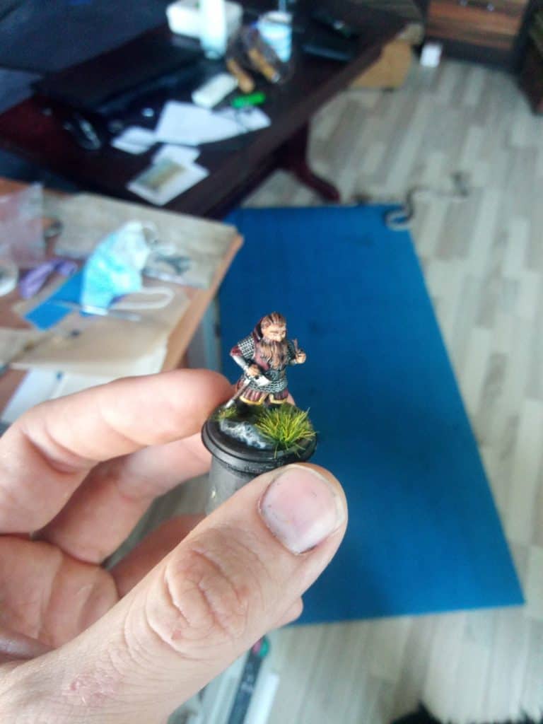 A hand keeping a painted 3d miniature of a dwarf standing on the grass 